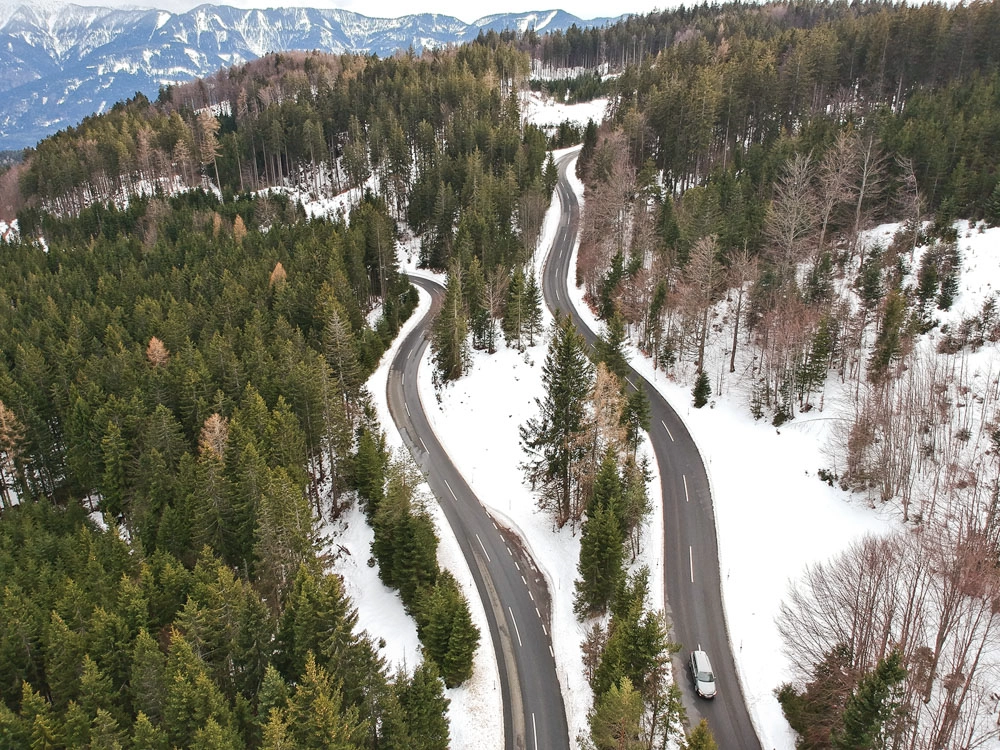 Drohnenfoto – Dobratsch Villach, Wald und Bergstraße in winterlicher Stimmung.