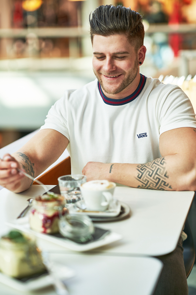 Gast genießt Dessert im Glas; daneben Cappuccino auf Untertasse – Sitzbereich im Restaurant Al Dente im Atrio Villach.