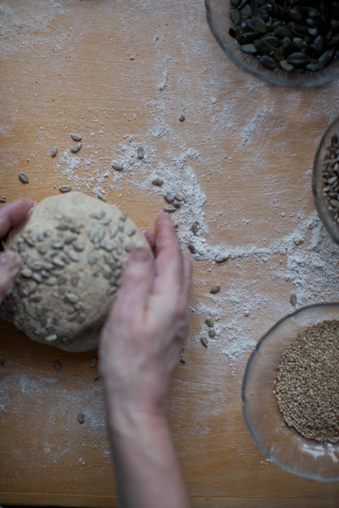 Brotteig mit Sonnenblumenkernen auf bemehlter Arbeitsfläche; Schalen mit Kernen daneben.