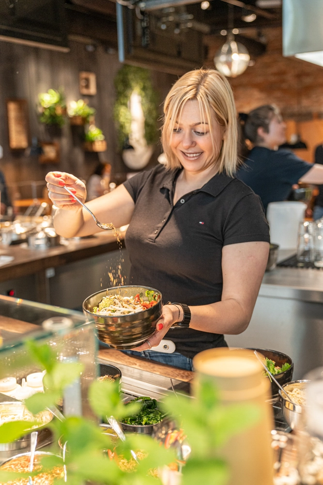 Mitarbeiterin richtet eine Bowl an und streut Zutaten darüber im My Indigo Restaurant, Atrio Villach.
