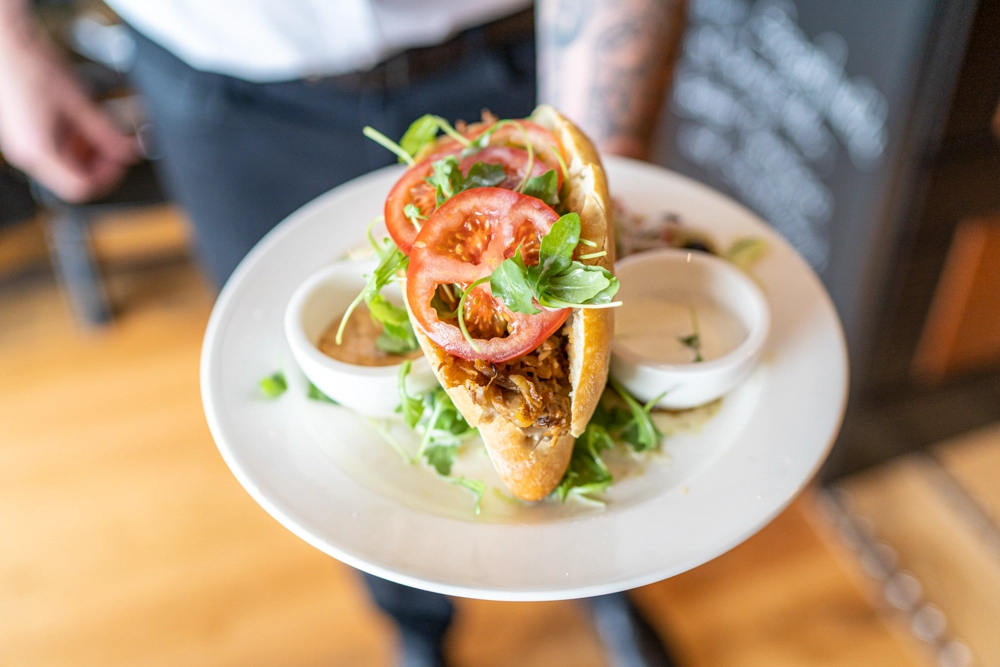 Sandwich mit Tomaten und Rucola auf weißem Teller, zwei Dip-Schälchen; serviert im Restaurant Augustin, im Atrio Villach.