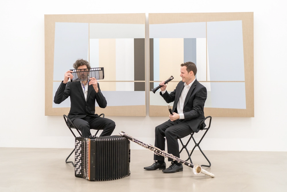 Werbefoto Duo-Klak – beide Musiker sitzend vor Kunstwerk; Akkordeon und Bassklarinette spielerisch in Szene gesetzt.