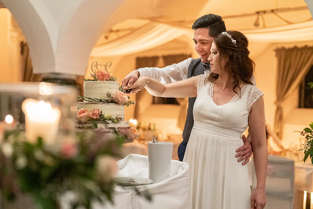Lachendes Hochzeitspaar schneidet bei Kerzenlicht eine wunderschöne Hochzeitstorte im Thon 7 Grafenstein, Kärnten auf – romantische Hochzeitsfotografie in Kärnten von Der mobile Fotograf & Videograf