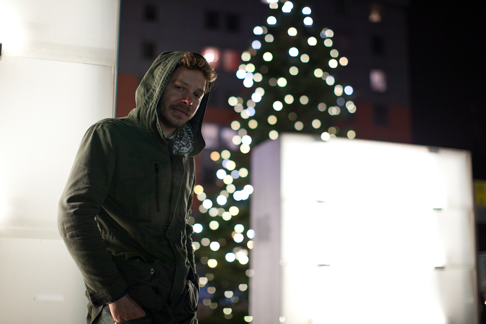 Porträtaufnahme – natürliche Peoplefotografie, Outdoor am Villacher Bahnhof zur Weihnachtszeit mit Weihnachtsbaum im Hintergrund.