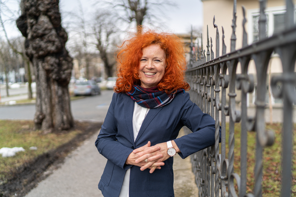 Business Porträt von Mag Isabella Scheiflinger vor der Anwaltschaft für Menschen mit Behinderung in Klagenfurt – Lanschaft im Hintergrund mit Park und Bäumen.