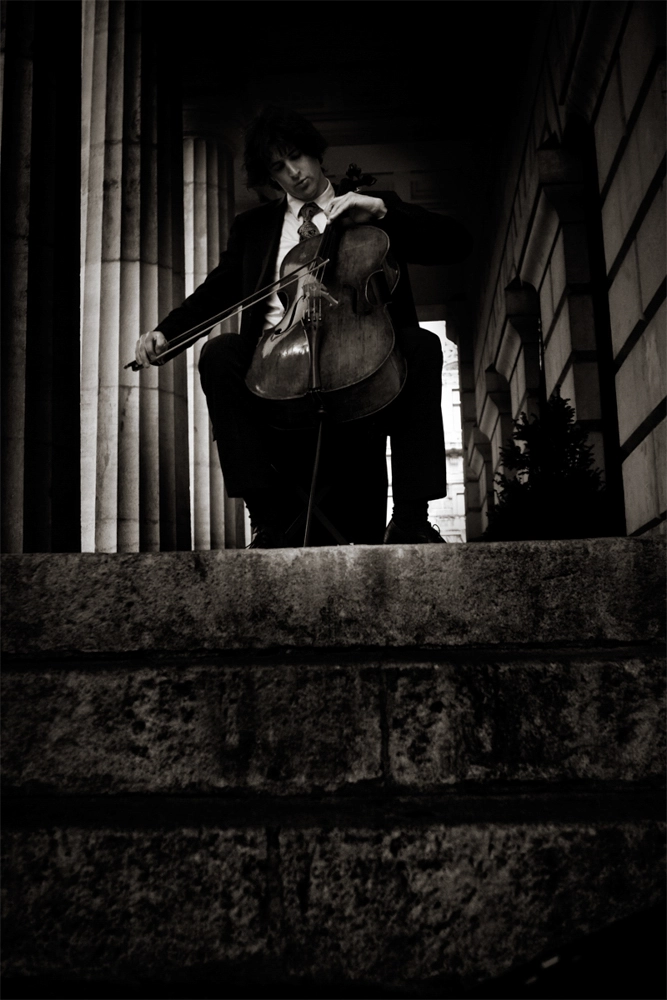 Werbefoto Peter Profant mit Cello auf Steinstufen zwischen Säulen – dramatische Schwarz‑Weiß‑Inszenierung in Wien.