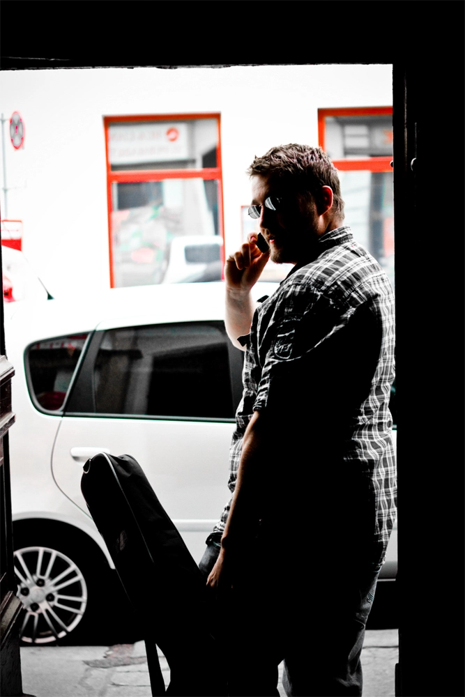 Business Porträt Musiker mit Sonnenbrille und Gitarrenkoffer am Eingang einer Wiener Straße.