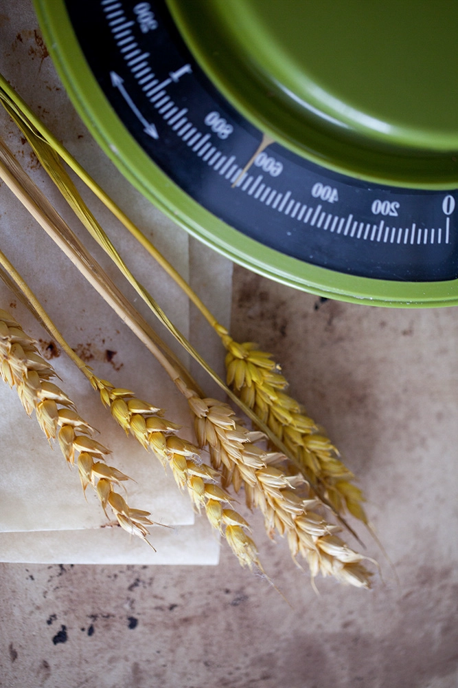 Getreideähren neben einer grünen Küchenwaage – rustikale Food-Stilllebenaufnahme.