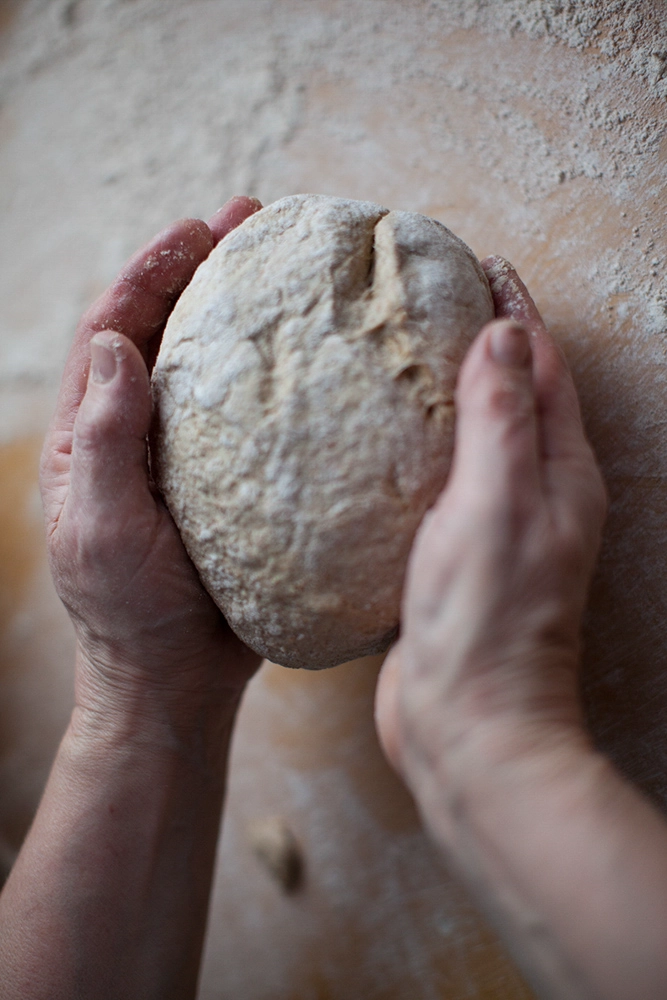 Beide Hände formen einen bemehlten Brotteiglaib.