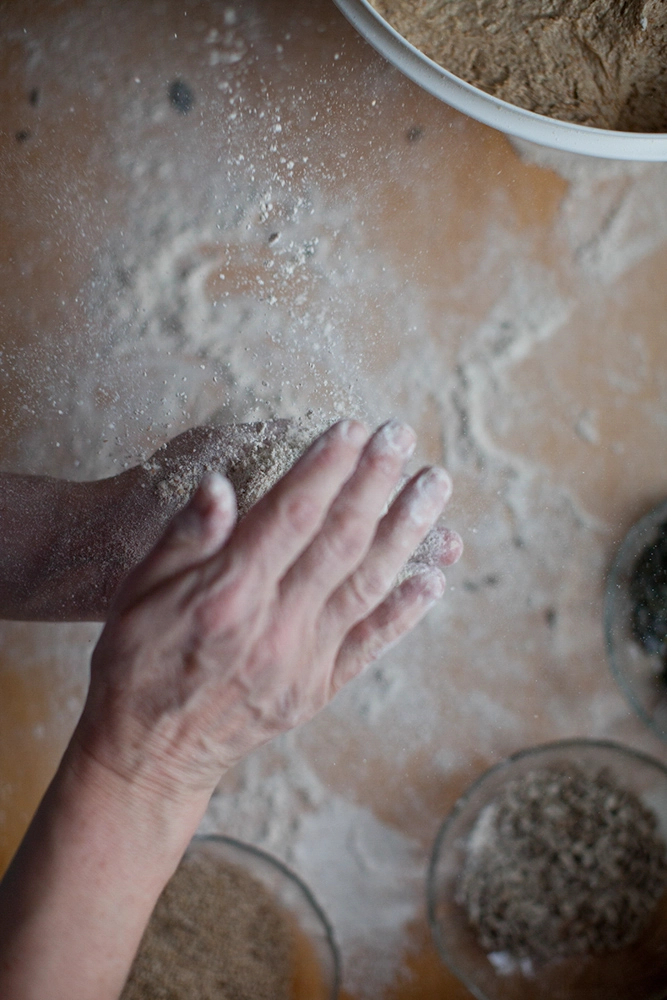 Mehlstaub wirbelt auf; Hände klopfen Teig ab – Backvorbereitung in Nahaufnahme.
