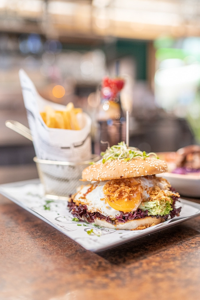 Streetfood-Burger mit Spiegelei im Sesambrötchen; daneben Pommes im Drahtkorb – Franz Streetfood Restaurant im Atrio Villach.